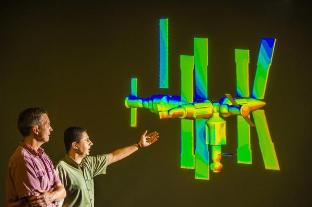Sandia National Laboratories researchers Steve Plimpton, left, and Michael Gallis look at a projection of a model of the Russian MIR space station, which fell out of orbit several years ago and disintegrated, with the remains ending up at the bottom of the Indian Ocean. Using Sandia’s 3-D code SPARTA, the calculation is simulating an instance of the process of de-orbiting. (Credit: Randy Montoya)