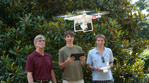 Reed Beverstock (right) pilots the physics department quadcopter while Daniel Duane (center) monitors the video feed on a computer tablet while Professor of Physics Bill Cooke looks on. They’re using the device to create video tutorials as part of a Creative Adaptation initiative. (Credit: Joseph McClain)